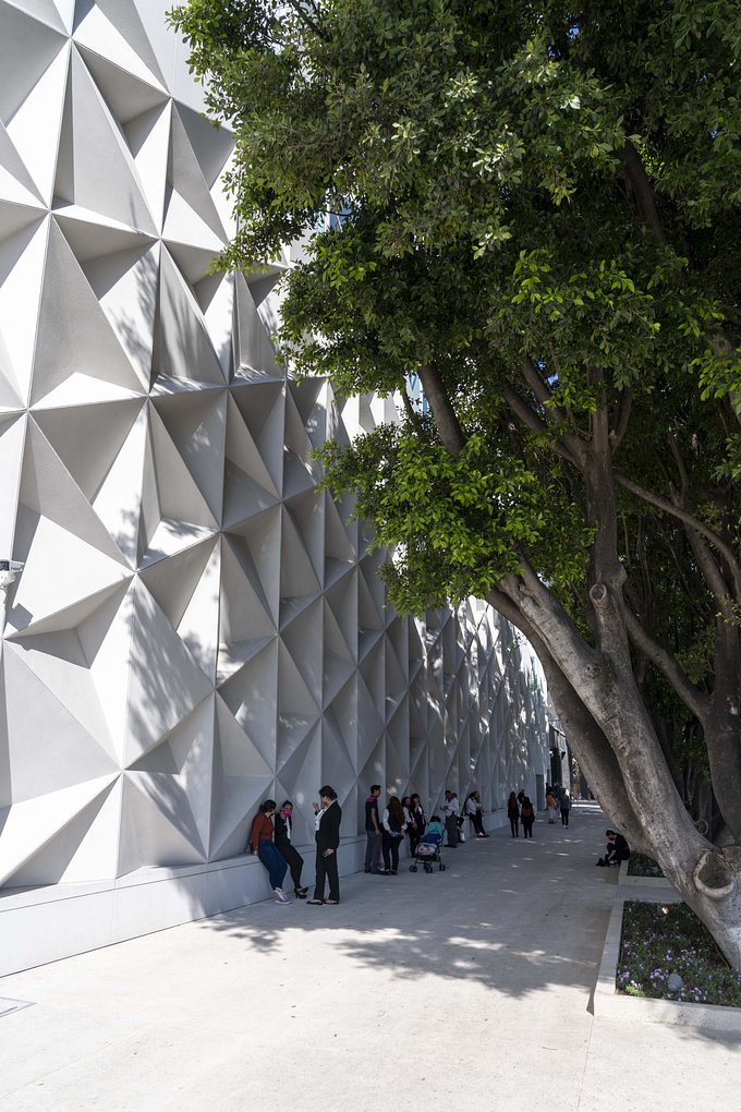 The project is located in the La Perla Shopping Center District, in the City of Zapopan, Jalisco, Mexico. It is an exercise in urban integration that combines modernity through architecture and tradition in the activities of the community in Jalisco.

The facade converges at a vertex that forms the union of two avenues, it is formed by a grid of triangular modules with flat pieces and in low relief, forming a subtracted pyramid, which when rotated allows multiple variables, and when combined it manages to transmit the sensation of movement. The texture rotates along the walls of the façade, which points to and accentuates the main access to the store. In addition to the set of reliefs, the same geometry has been transferred to the openings through windows that frame the exterior urban context and allow natural lighting inside.

The intention of this facade is that as the day passes, the solar illumination generates games of shadows and reflections. Therefore, the facade always looks different, even at night, thanks to the lighting design. It is important to point out that the scale of the project was decisive for the modulation, the composition responds to the large canvas of the envelope, without losing sight of the user, it is interesting to observe in an open view how the human figure is embraced by the games of lines and their own shadows.

The facade construction is made from prefabricated white concrete on metal frames, the material allows minimal maintenance, and being a designed piece allows the least number of adjustments in placement.